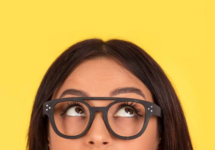 closeup portrait headshot cropped face above lips of cute happy woman in glasses looking up isolated on yellow studio wall background with copy space above head. Human face expressions, emotions